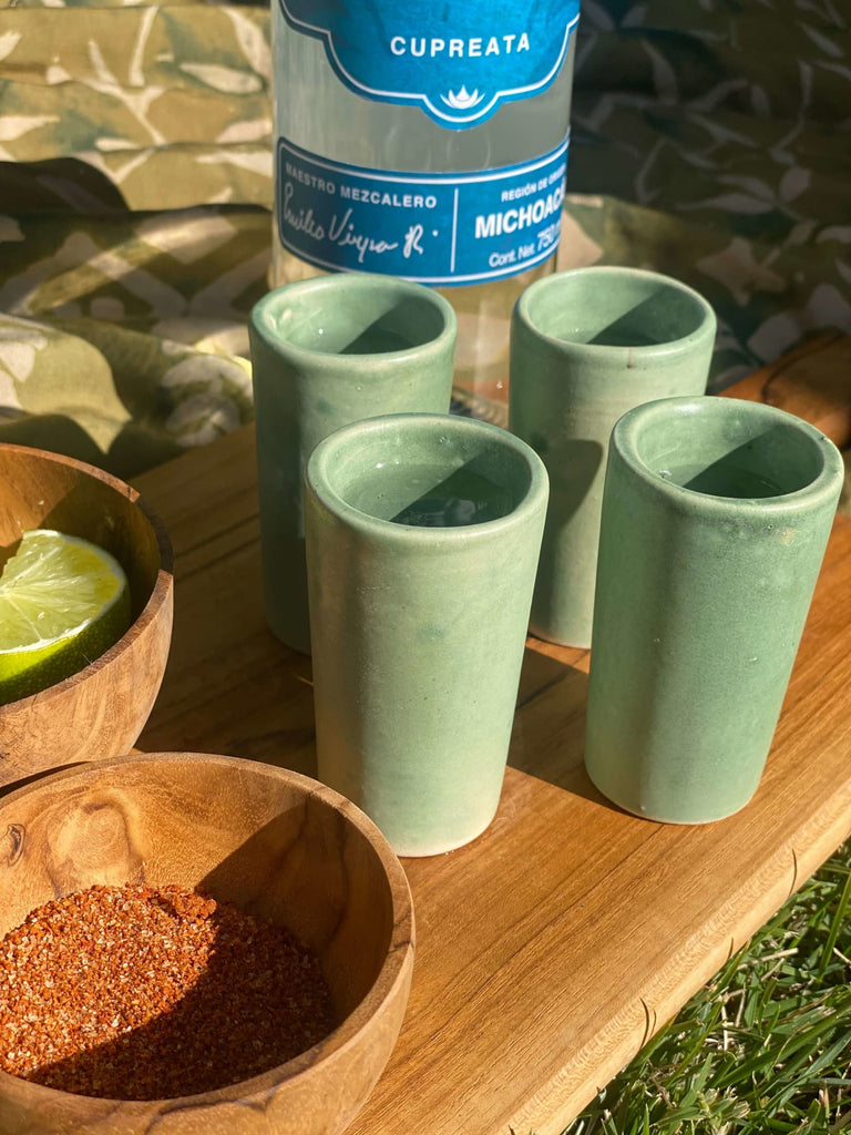 set of four green high fire clay shot glasses with lime and chili powder in a wooden bowl on a wooden board