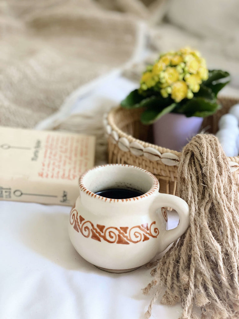 beautiful high fire clay white mug with brown tribal design filled with black coffee on bed with other boho chic decor