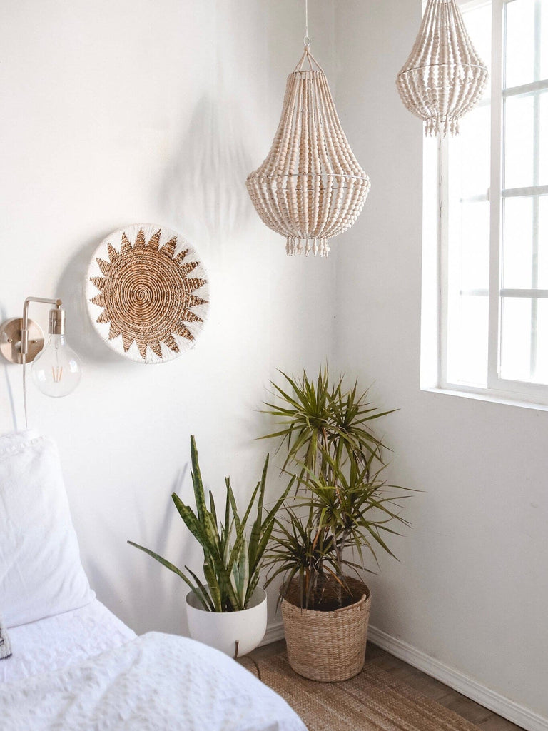 natural wooden bead chandeliers next to woven wall basket hanging over plants in a modern bohemian bedroom corner