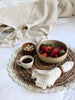 banana bark placemat with macrame crochet trim detail holding bowl of strawberries, espresso mug, teak wood with nuts and linen napkin