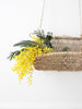 closeup of bohemian handwoven hanging wall basket holding dainty yellow flowers with a white background
