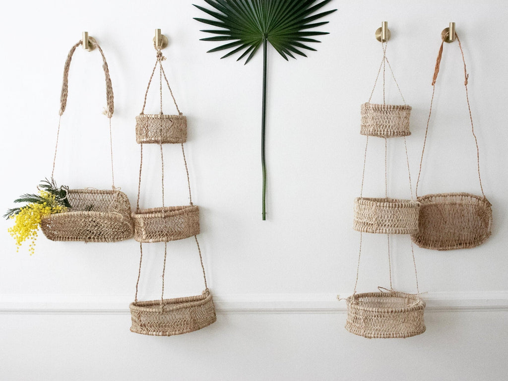 two single cottagecore wall baskets and two trio bohemian wall baskets hanging on white wall with palm leaf