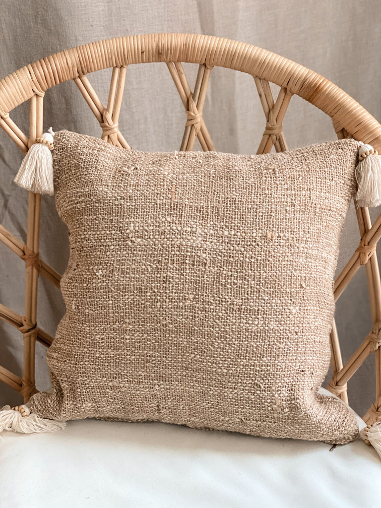 decorative bohemian handwoven jute throw pillow with cream tassels for scandi boho decor on wicker chair