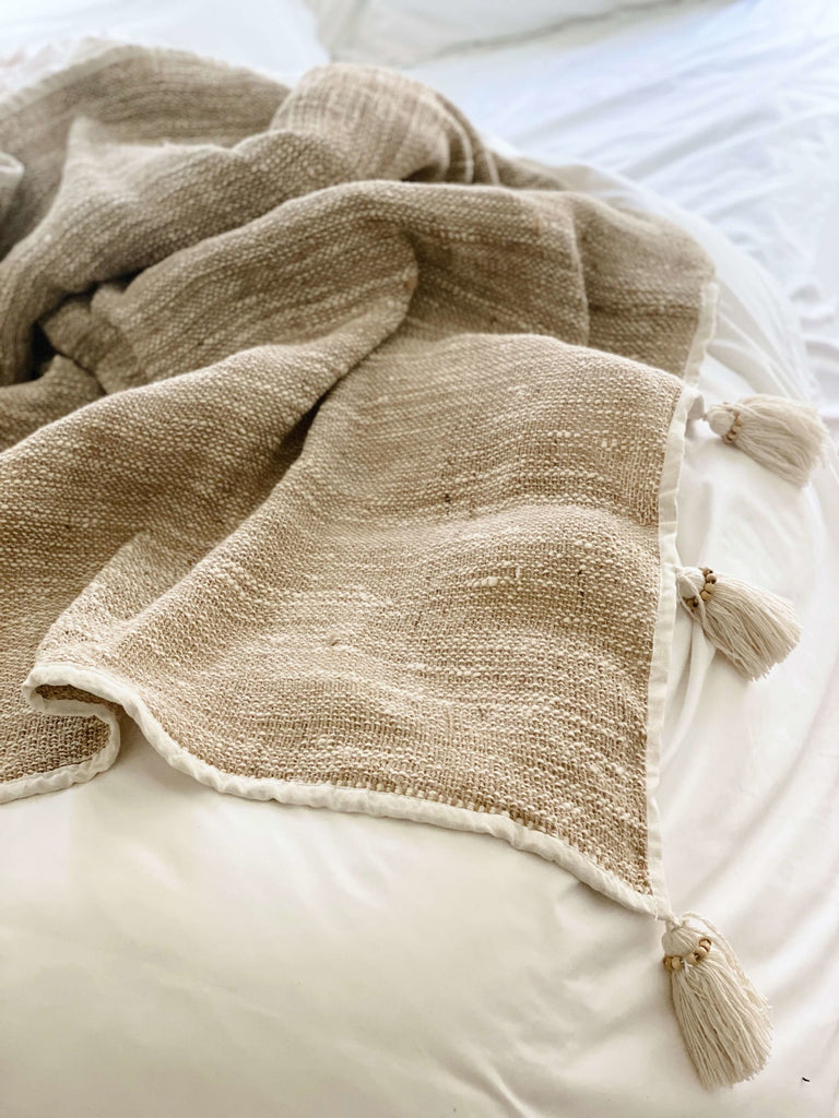 bohemian handwoven jute and linen cream cozy throw blanket with tassels on white bedding