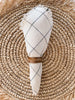 handwoven white and navy checkered linen napkin set held together by napkin ring displayed on straw fringe coaster