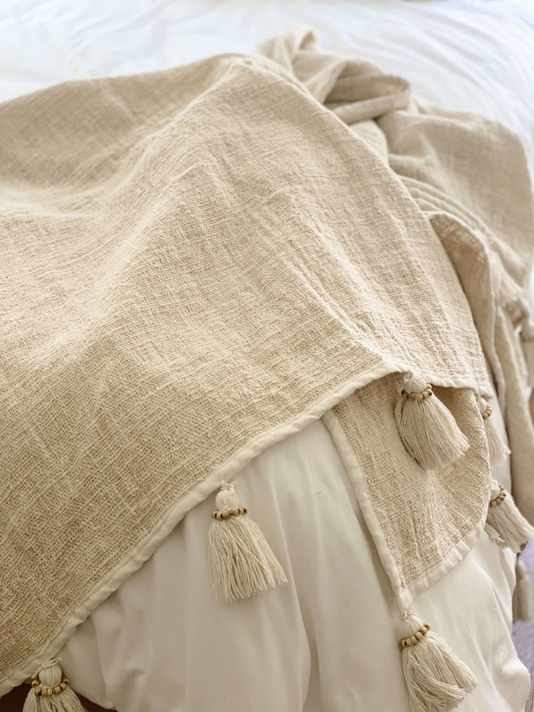 handwoven jute and linen cream cozy throw blanket with tassels used as a natural bohemian bedroom accent