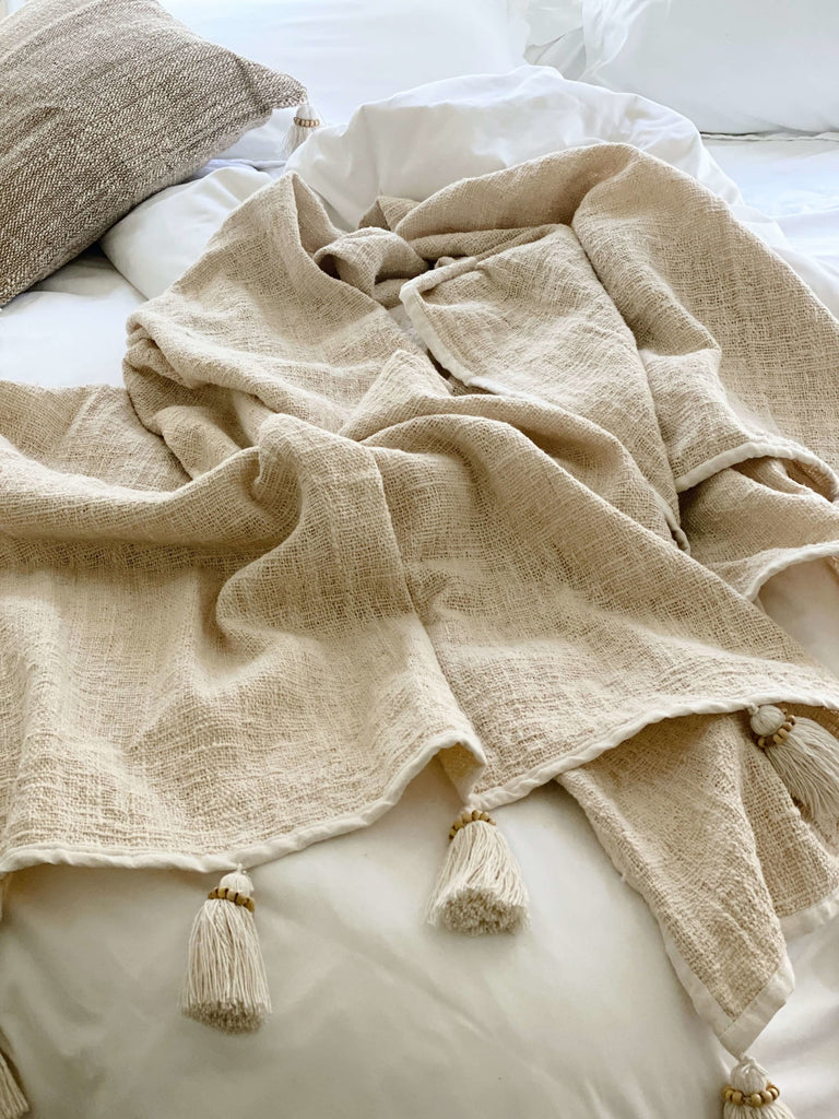 natural handwoven jute and linen cream throw blanket with tassels on a cozy bohemian earth inspired bed