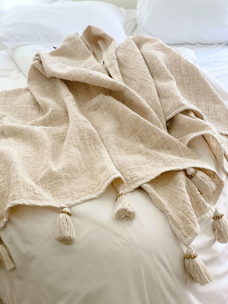 natural bohemian handwoven jute and linen cream cozy throw blanket with tassels on a white bed in modern boho bedroom