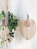 large natural bohemian handwoven palm leaf fan hanging on white wall next to macrame plant hanger with pothos