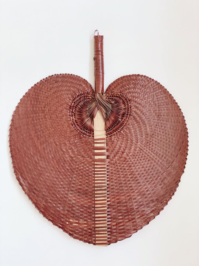 product photo of large burgundy bohemian handwoven palm leaf fan hanging on white wall