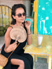 girl in bohemian cafe cooling off with handwoven palm leaf fan and coconut shake