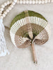 small white, brown, and olive handwoven palm leaf fan next to natural bohemian wooden bead tassel