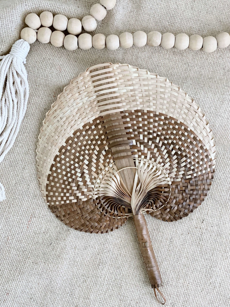 small natural brown handwoven palm leaf fan next to natural bohemian wooden bead tassel