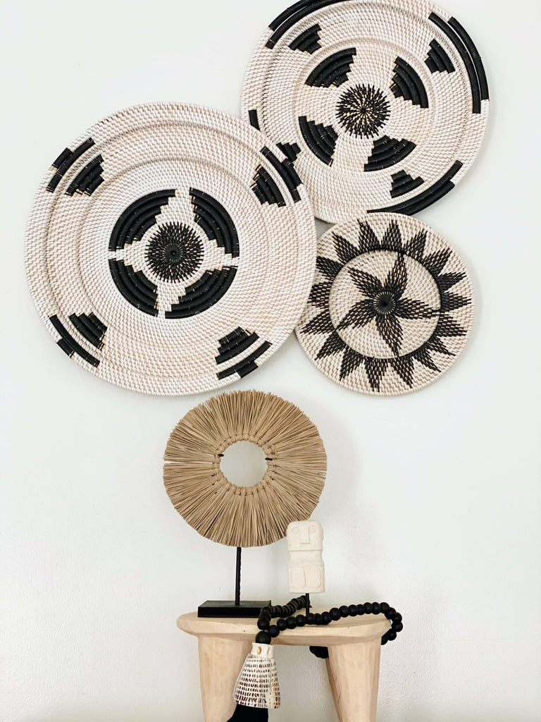 trio of handwoven black and white wall basket cluster hanging on top of african stool holding black tassel and timor statue