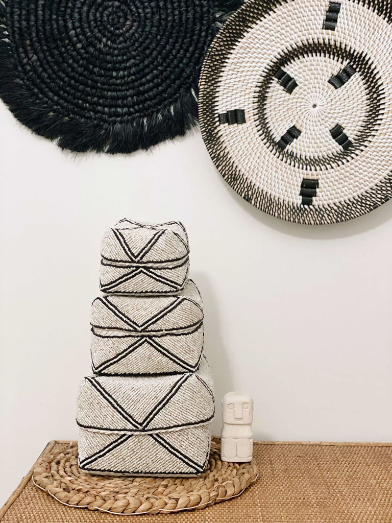 black and white handwoven rattan wall basket next to a trio of beaded black and white bamboo baskets