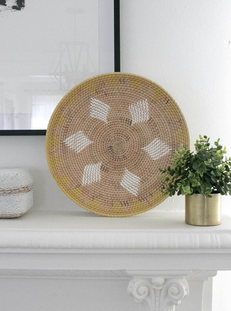natural yellow handwoven rattan wall basket on top of mantel next to luscious green plant and white beaded bamboo basket