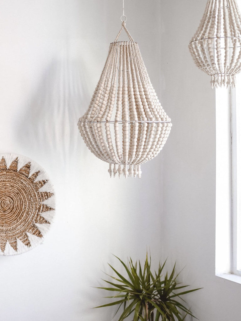 handwoven seagrass wall basket in modern bohemian bedroom next to white wooden bead chandeliers