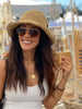 a happy and fashionable bohemian woman wearing a straw bucket hat on a warm, sunny day