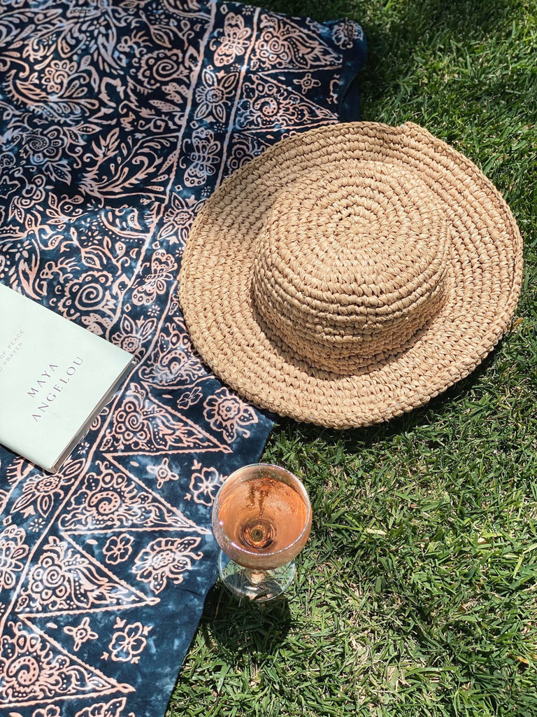 hand-woven straw bucket hat next to glass of rosé and book on a beautiful sunny picnic day