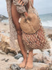 girl in bohemian beach fashion holding beaded fishnet tote bag with palm leaf fan at the beach