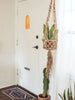 brown beaded jute plant hanger holds terra cotta planter in boho style entryway with snake plant and cactus