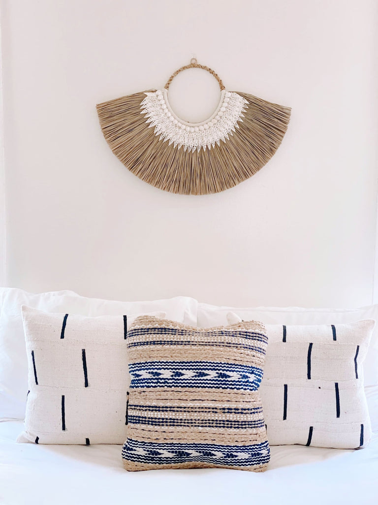 beaded grass fan wall hanging on top of bed with african mudcloth pillows in modern bohemian bedroom