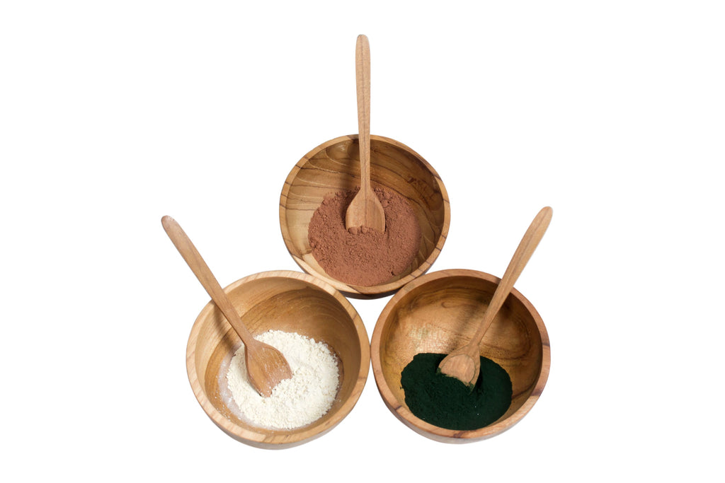 trio of mini handcarved teak wood bowl and spoon set with colorful spices on white background