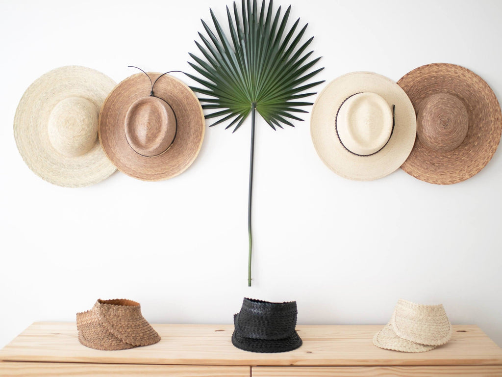 bohemian palm leaf hat collection hanging on white wall with palm leaf and palm leaf sun visors on dresser