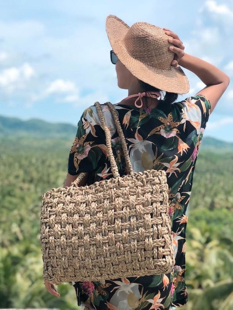 tourist wearing a handwoven brown palm leaf sun hat and straw bag on a sunny day at a beautiful countryside location