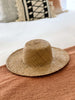 handwoven bohemian brown palm leaf sun hat on bohemian bed with macrame pillows