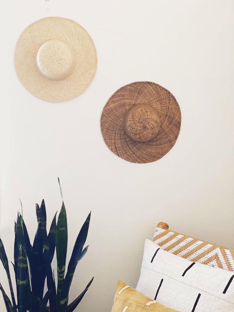 set of two bohemian palm leaf summer hats hanging on top of rattan lounge chair with african mudcloth pillows