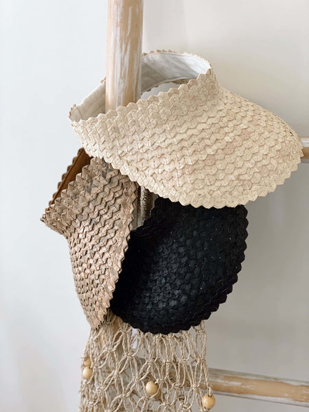 trio stack of cream, black, and brown palm leaf sun visors on wooden ladder with beaded fishnet market tote bag