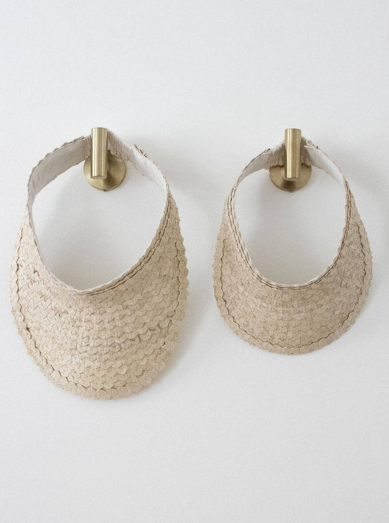 set of two regular and mini handwoven vanilla cream palm leaf sun visor hanging on gold hooks on white wall