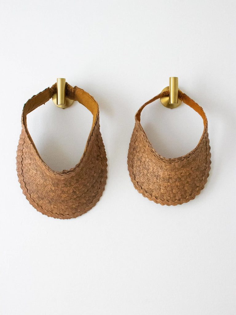 set of two regular and mini handwoven brown palm leaf sun visor hanging on gold hooks on white wall