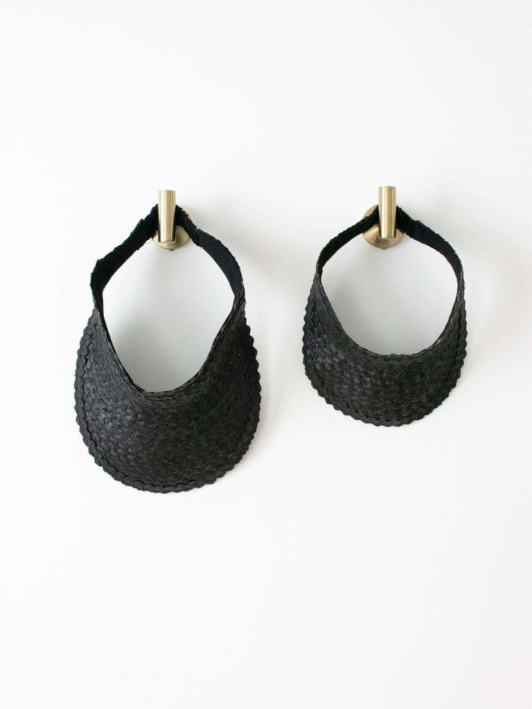 set of two regular and mini handwoven black palm leaf sun visor hanging on gold hooks on white wall