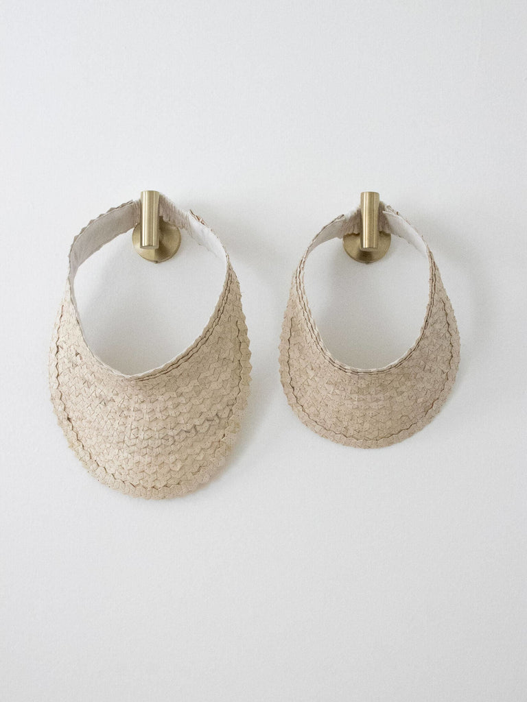 set of two regular and mini handwoven vanilla cream palm leaf sun visor hanging on gold hooks on white wall