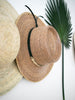 closeup of bohemian handwoven palm leaf brown sombrero with black and gold accent hanging on white wall with palm leaf 