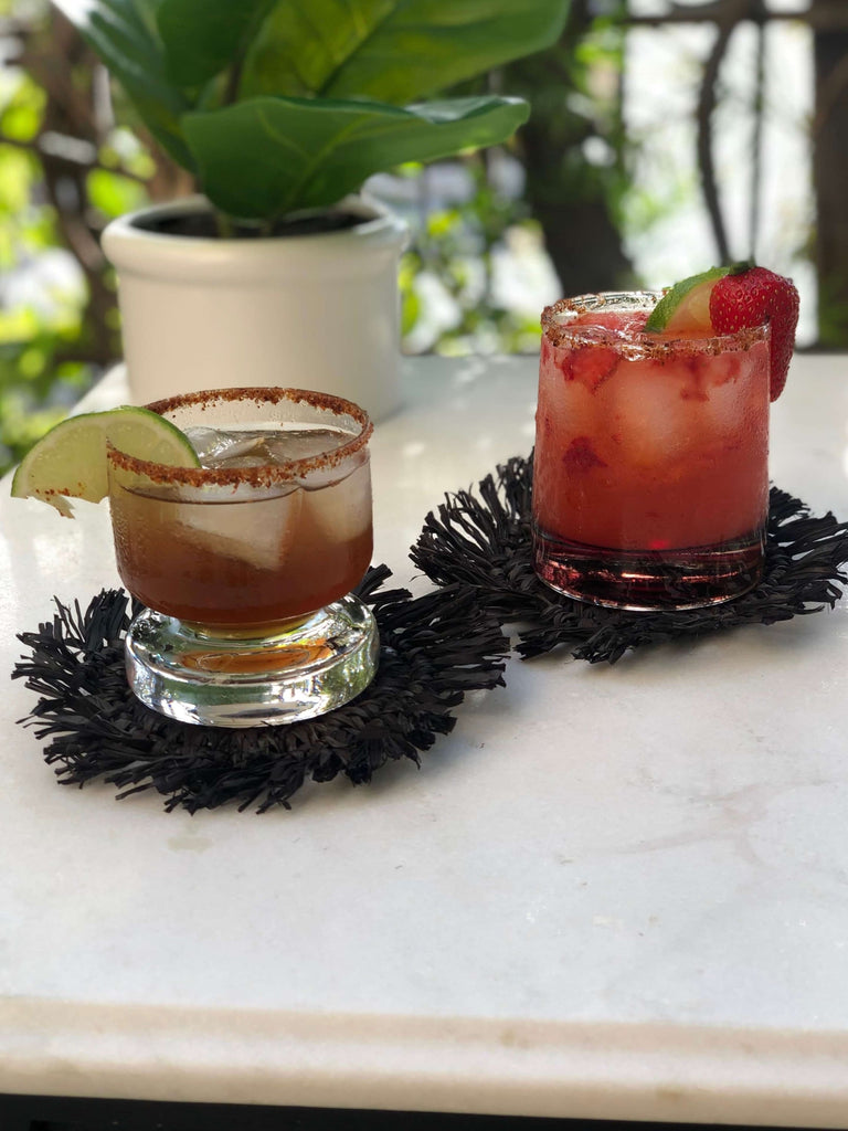 black woven fringe coasters with delicious alcoholic drinks next to plants during happy hour