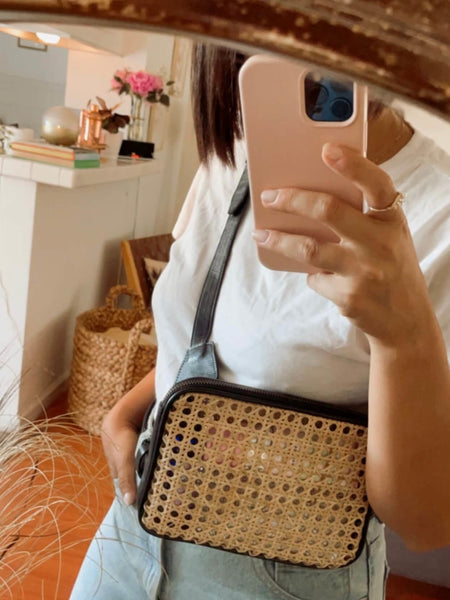woman taking mirror selfie in entryway wearing a black leather and rattan crossbody fanny pack