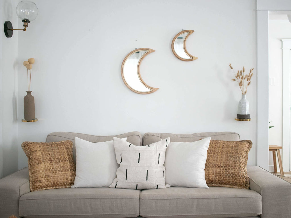 pair of crescent moon wicker mirrors above gray couch with african mudcloth pillows in beautiful bohemian minimalist living room