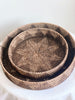 set of two brown bohemian handwoven rattan nesting trays laid on top of each other on white cloth table