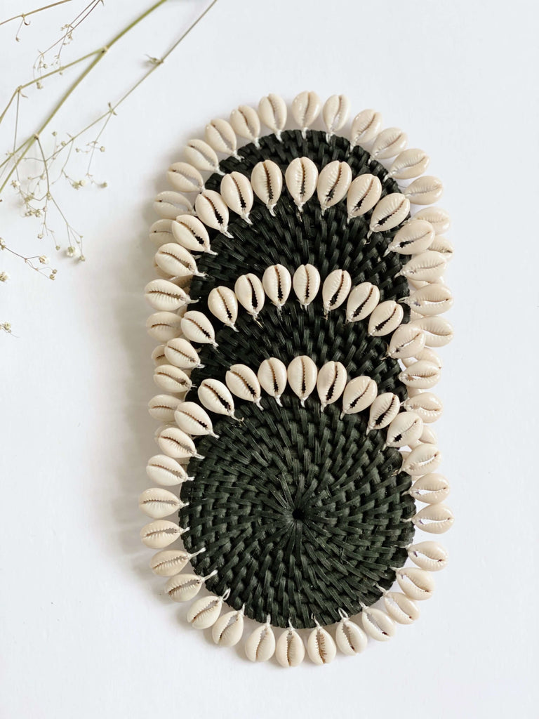 set of four handmade black rattan coasters that are adorned with a beautiful cowrie shell detail next to baby's breath florals