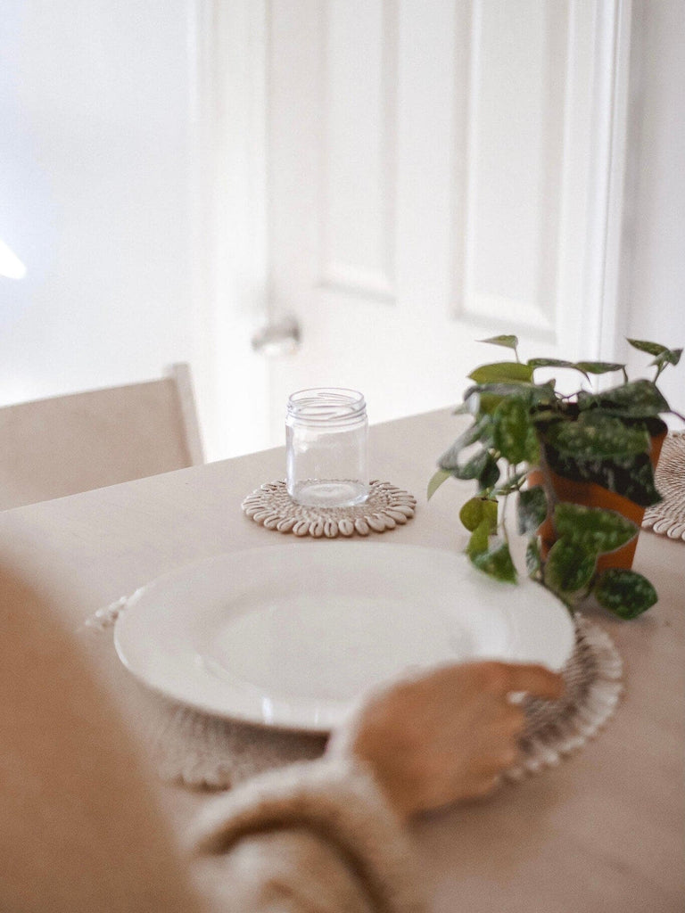 woman setting the dining table with bohemian rattan shell placemats and coaster with pothos plant centerpiece