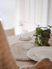 woman setting the dining table with bohemian rattan shell placemats and coaster with pothos plant centerpiece