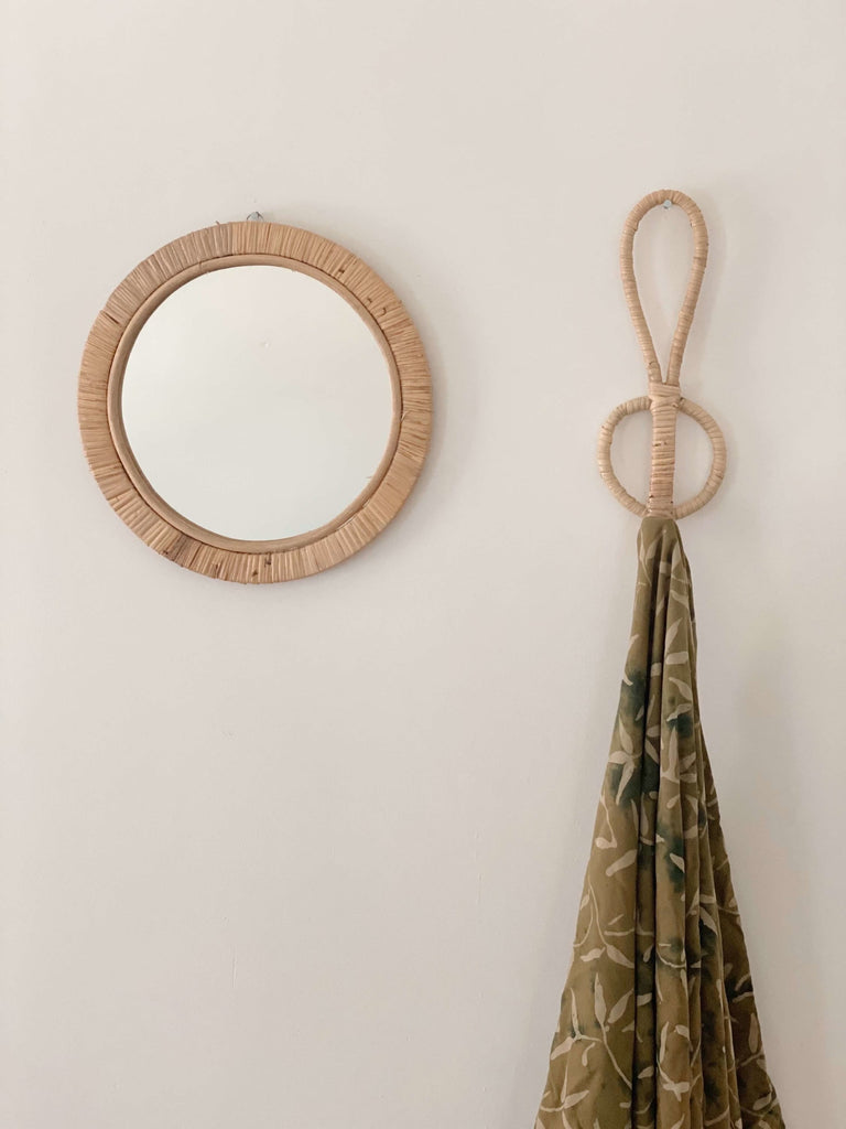 white wall with handmade rattan wicker home decor including rattan mirror and single wooden hook