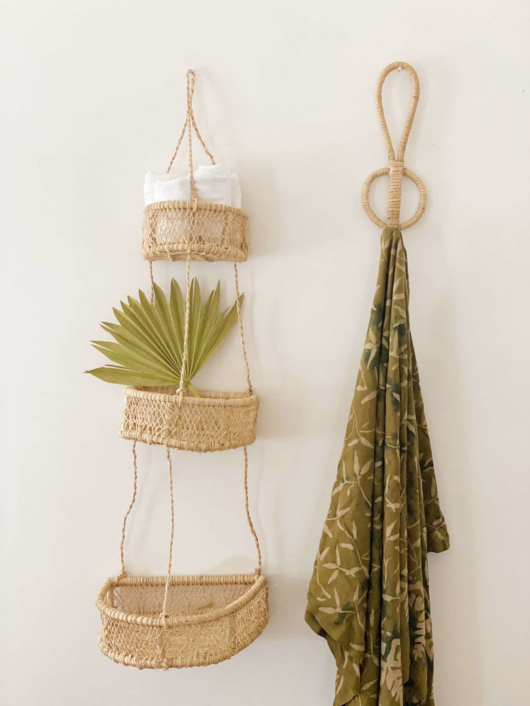 single rattan wall hook holding detailed green scarf next to handwoven trio hanging wall basket with palm leaves