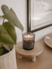 closeup of natural wooden riser holding lit candle next to a small monstera plant in woven pot