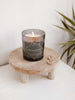 small natural wooden candle riser with lit candle and pair of gold earrings on white dresser