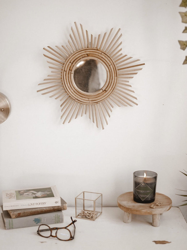 bohemian academia dresser setup with mini wooden riser with candle, stacked books, and hanging rattan sunshine mirror