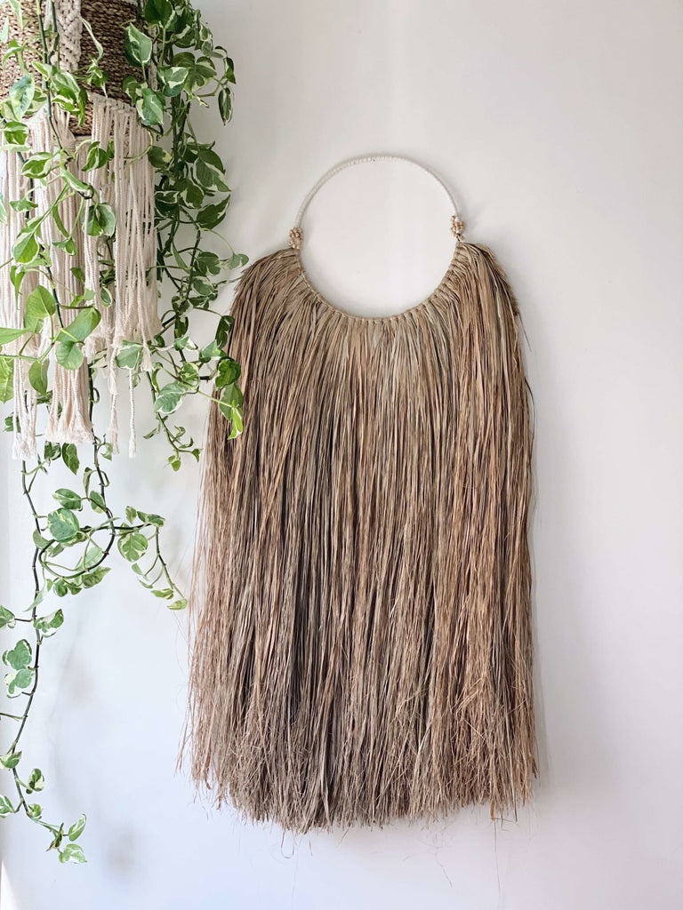 minimalist rustic seagrass wall hanging next to lush hanging plant